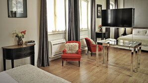 Una habitación de hotel moderna con una cama grande, un sillón rojo, un televisor y una ventana con cortinas.