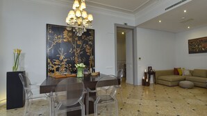 Comedor con candelabro, sillas traslúcidas, una mesa de madera oscura y un cuadro grande con motivos florales en la pared.