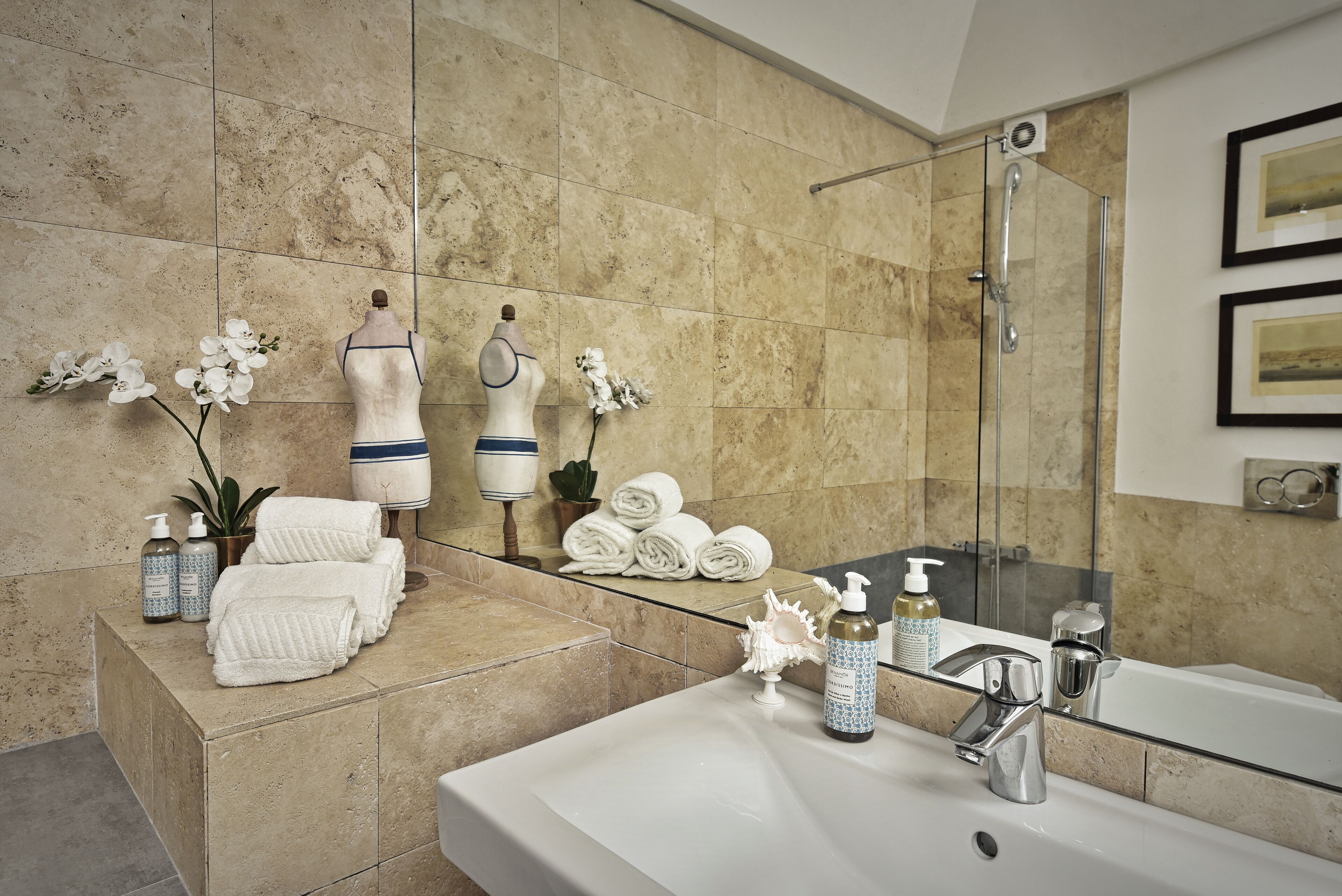 Une salle de bain dotée d’un grand lavabo, d’une douche en verre et d’un meuble-lavabo avec des serviettes et des articles de toilette.