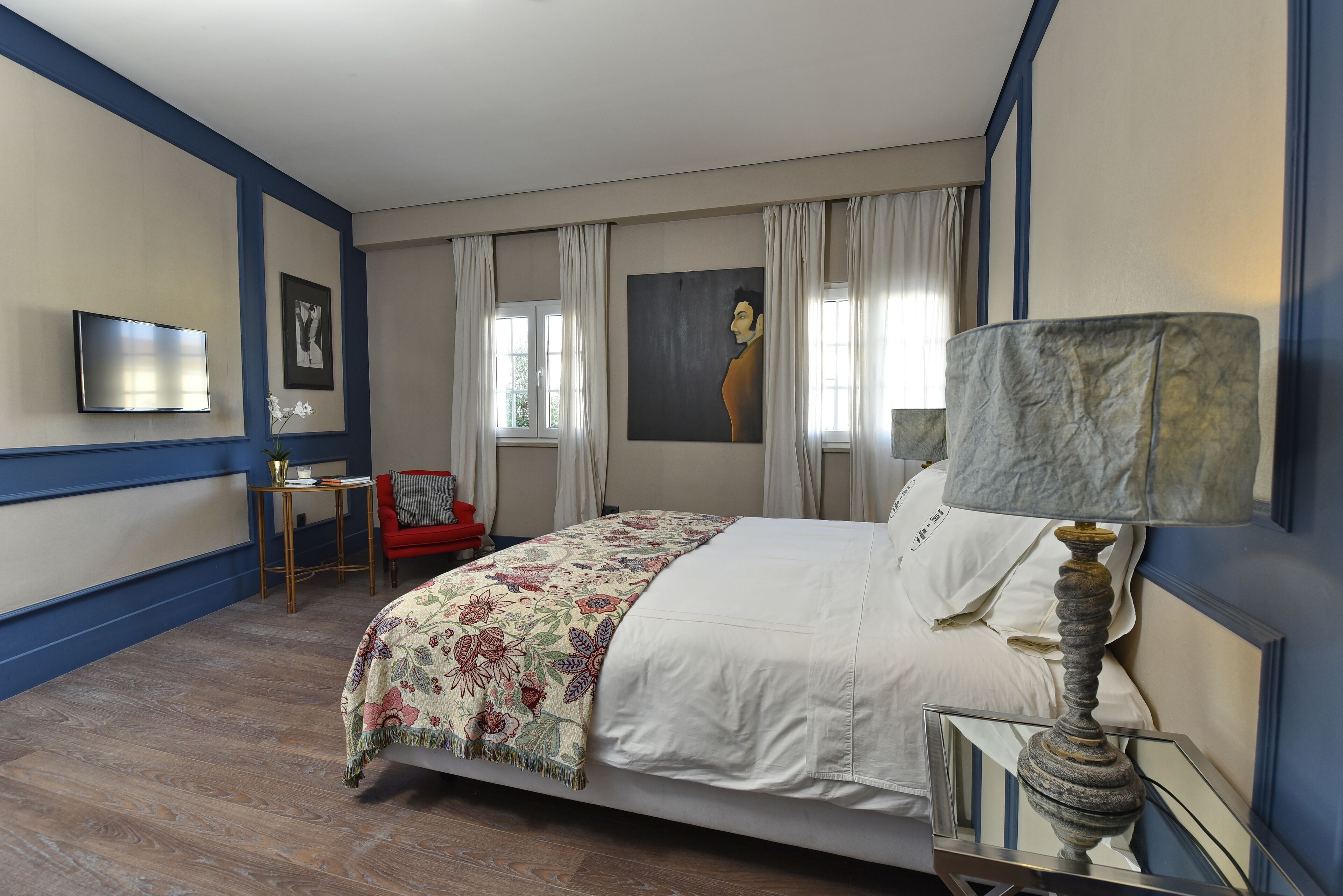 Een slaapkamer met een bed, een televisie, een rode stoel en een schilderij aan de muur.