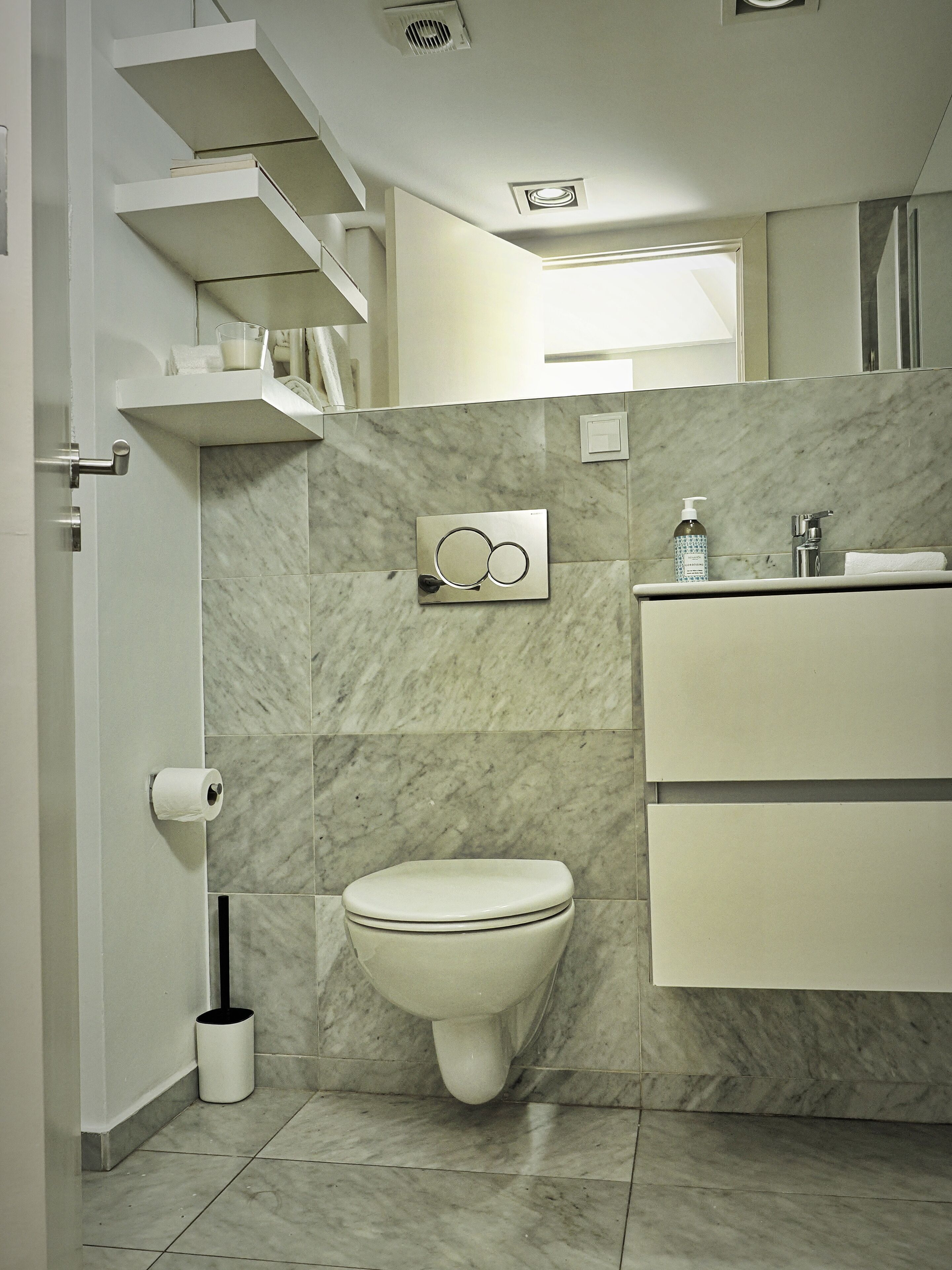 A modern bathroom with a toilet, a sink, and a shower. There are marble tiles on the walls and floor.