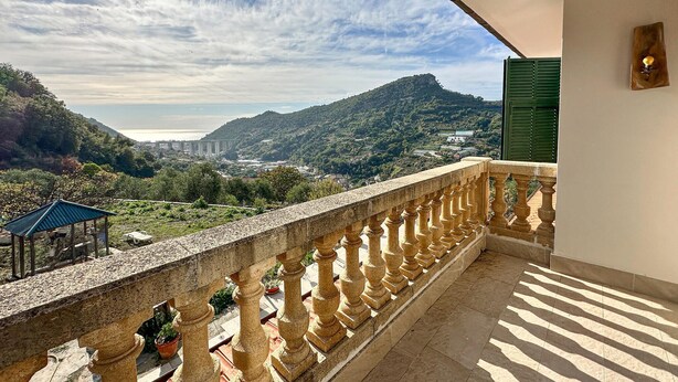 Un balcone con ringhiera in pietra che si affaccia su un panorama suggestivo: un ponte, delle colline e una distesa d'acqua.