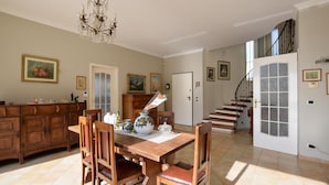 Un'ampia sala da pranzo con tavolo e sedie in legno, un lampadario e una scala che conduce a un altro piano.