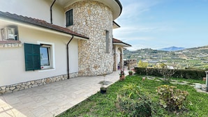 Una casa con facciata in pietra, un patio piastrellato e vista su un paesaggio collinare.