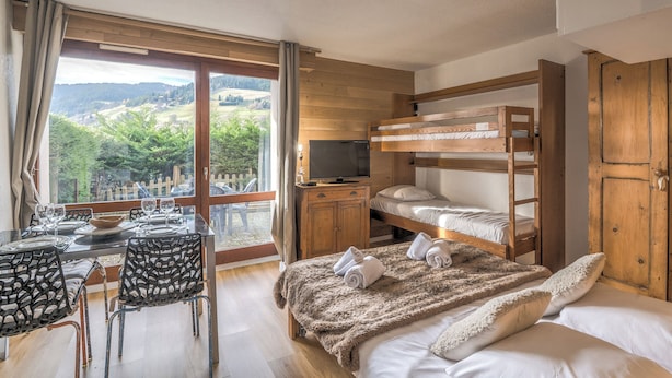 Una stanza con un letto a castello, una televisione, un tavolo da pranzo con sedie e vista sull'esterno.