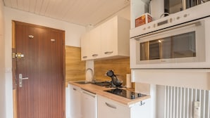Una cucina compatta con una porta in legno, mobili bianchi, forno a incasso e lavastoviglie.