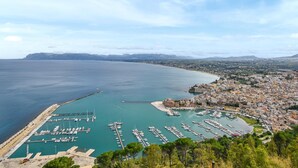 A coastal town with a marina, buildings, and a mountainous backdrop.