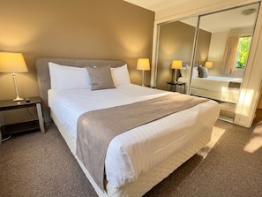 Ein Hotelzimmer mit einem großen Bett, Nachttischlampen, einem Spiegel und Teppichboden.