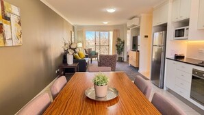 Een moderne keuken met witte kasten, roestvrijstalen apparatuur en een eethoek met een houten tafel en stoelen met kussens.