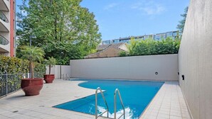 Una piscina con una pequeña zona de terraza, rodeada por un muro bajo y plantas en macetas.