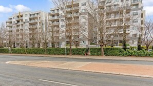 Ein mehrgeschossiges Wohngebäude mit Balkonen, eine gepflasterte Straße davor und ein klarer Himmel.