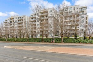 Ein mehrgeschossiges Wohngebäude mit Balkonen, eine gepflasterte Straße davor und ein klarer Himmel.