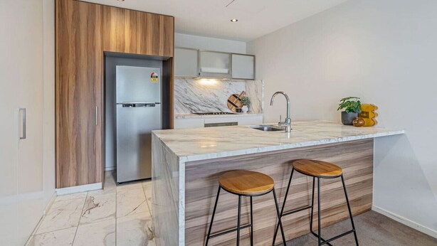 Eine moderne Küche mit Marmorarbeitsplatte, Edelstahlgeräten, Holzakzenten und einer Bar mit Sitzgelegenheiten.