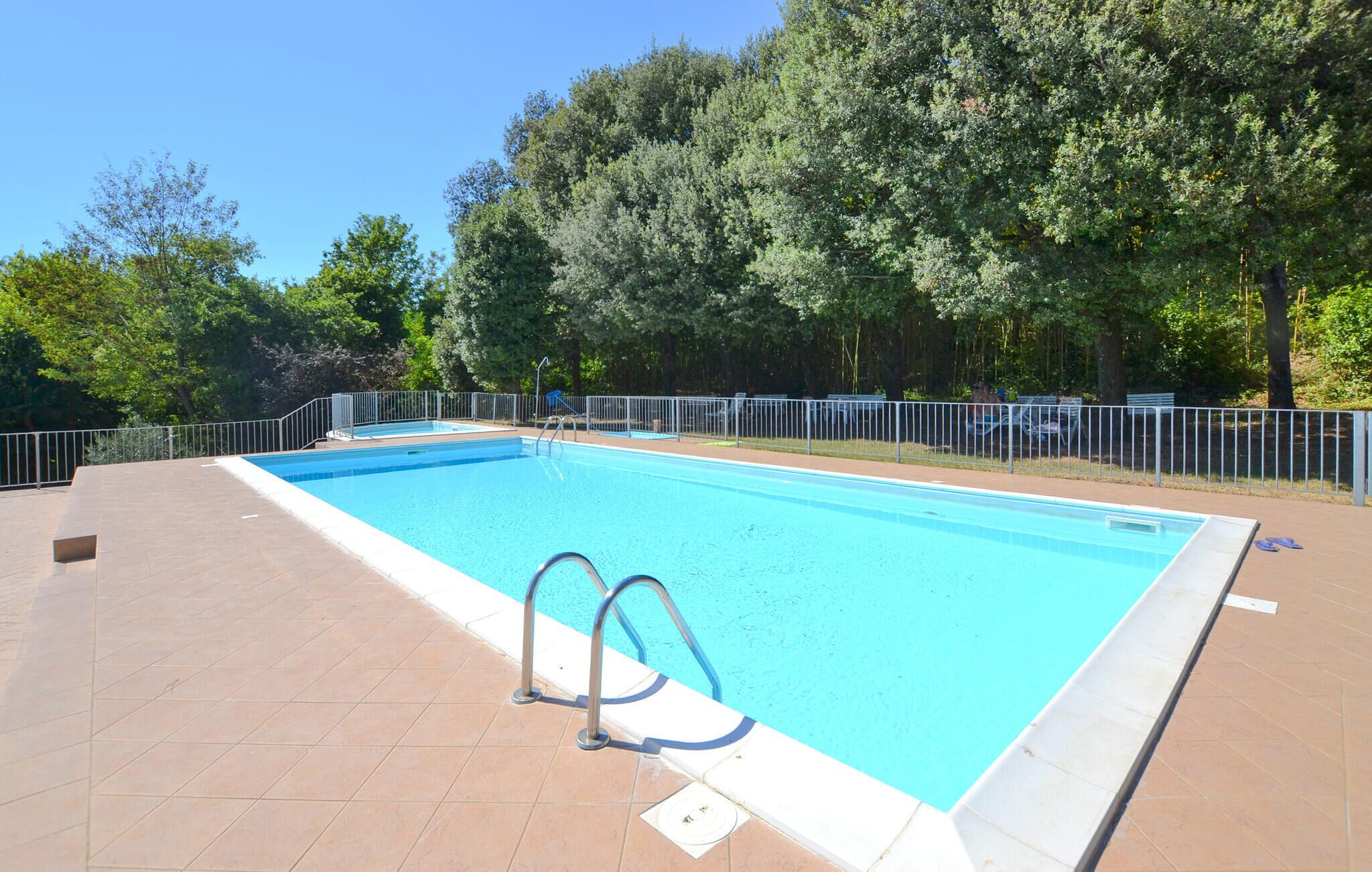 Une piscine rectangulaire avec un escalier en métal, entourée d’une clôture en métal et d’une terrasse carrelée.