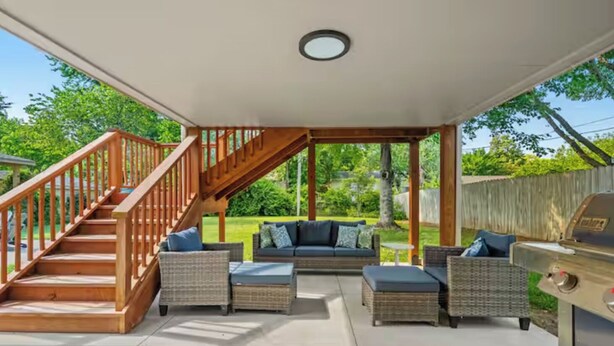 Une terrasse couverte avec un escalier en bois, des meubles en osier et un barbecue.