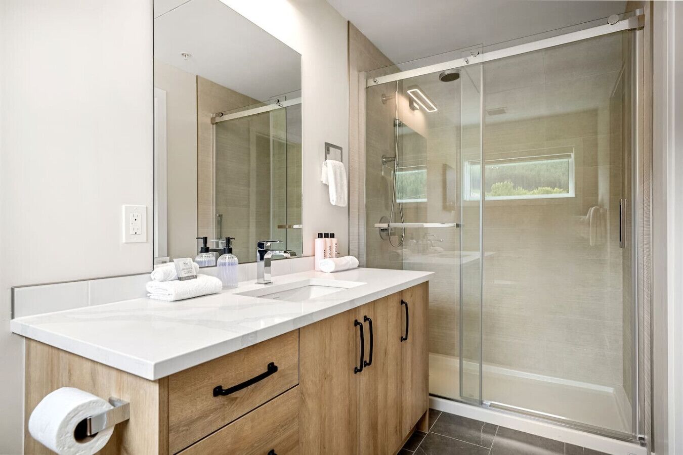 A modern bathroom with a white sink, wooden cabinet, and a glass shower enclosure.