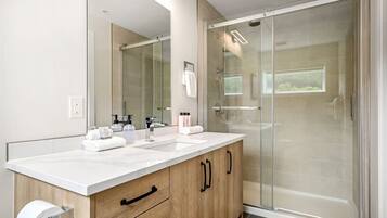 A modern bathroom with a white sink, wooden cabinet, and a glass shower enclosure.