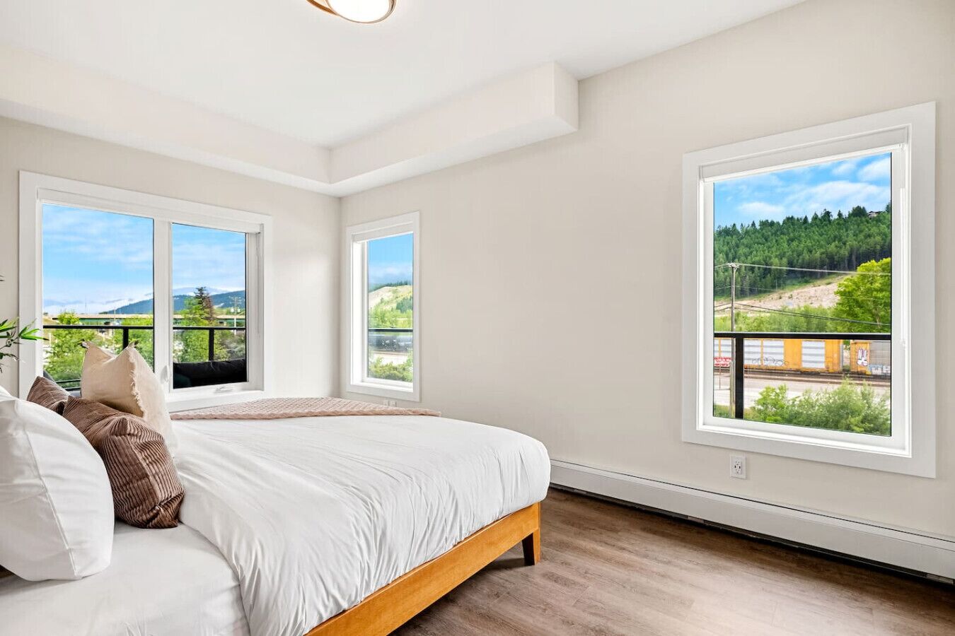 A bedroom with a large bed, two windows, and a view of a forest and train tracks.