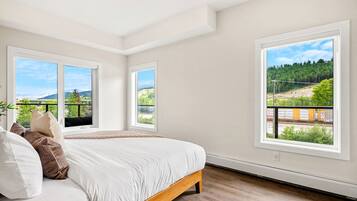 A bedroom with a large bed, two windows, and a view of a forest and train tracks.