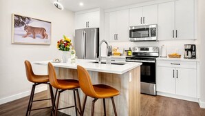 A modern kitchen with white cabinets, stainless steel appliances, and a central island with bar stools. - New 2BR in DT Golden AC, Balcony, BBQ, Sleeps 6 (Golden)