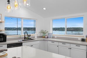 A modern kitchen with white cabinets, a large island, a view of a lake, and a coffee maker.