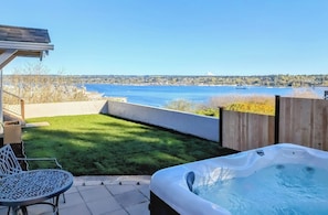 A hot tub, patio table, and chairs with a view of a body of water and distant mountains.