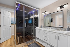 A modern bathroom with a glass shower enclosure, a large mirror, and a vanity with a marble countertop.