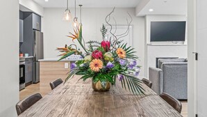 Ein moderner Essbereich mit Holztisch, Stühlen, einer Blumenvase und einer Küche im Hintergrund.