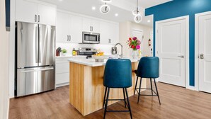 A modern kitchen with white cabinets, stainless steel appliances, a wooden island, and two blue bar stools.