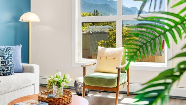 A room with a large window, a sofa, a chair, a lamp, and a plant.