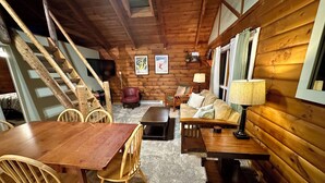 A cozy cabin interior with a wooden dining table, chairs, a sofa, and a staircase. - Lovely 2-Bedroom with Loft Condo at the Base of Snowshoe--a Perfect Getaway! (Snowshoe)