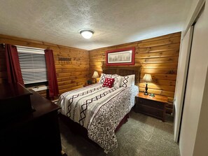 Une pièce chaleureuse avec un mur en bois, un lit recouvert d’une literie à motifs, deux lampes de chevet et un luminaire au plafond.