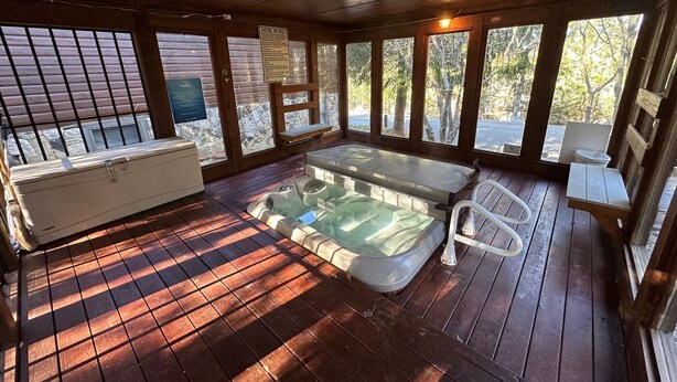A hot tub area with a wooden deck, a bench, and a view of trees through large windows. - Lovely 2-Bedroom with Loft Condo at the Base of Snowshoe--a Perfect Getaway! (Snowshoe)