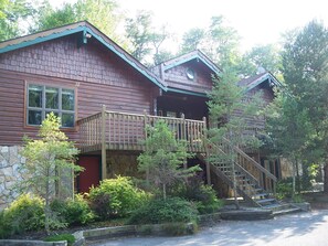 Une cabane en rondins avec des fondations en pierre, une terrasse en bois et un escalier menant à un balcon situé à l’étage.