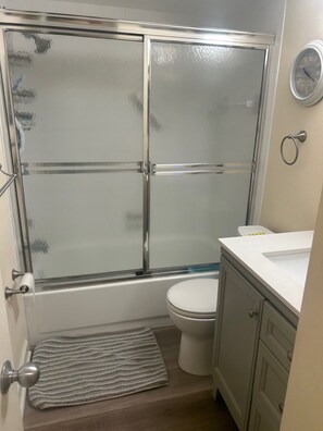 Ein Badezimmer mit Duschkabine, Toilette, Waschbecken und einer kleinen Fußmatte.