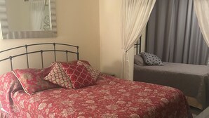 A bedroom with a bed, a bedside table, a ceiling fan, a window with curtains, and a mirror on the wall. - 2-bedroom condo in Sarasota 1 1/2 miles from beautiful Siesta Key (Sarasota)