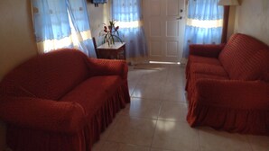 Ein Zimmer mit zwei roten Sofas, einem kleinen Tisch mit einer Vase und einer Tür mit Fenster.