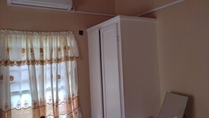 Ein Zimmer mit einem Fenster, das mit blumigen Vorhängen verziert ist, einer weißen Tür und einer Klimaanlage an der Wand.