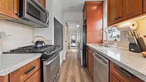 A kitchen with wooden cabinets, stainless steel appliances, a granite countertop, and a view into the dining area. - Private Hot Tub, Mini-Golf, Firepit, BBQ, 10 Mins to Zoo & Balboa Park (San Diego)