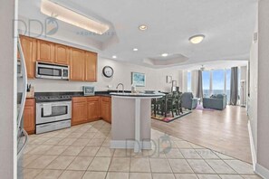 A modern kitchen with wooden cabinets, a central island, and a dining area with a view. - Beau View 1805 | The Perfect Long-Term Coastal Escape! (Biloxi)