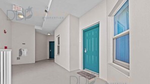 A hallway with a teal door, a window, and a welcome mat. - Beau View 1805 | The Perfect Long-Term Coastal Escape! (Biloxi)