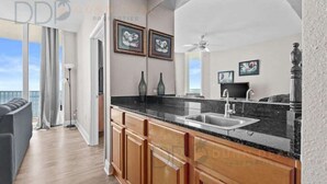 A modern kitchen with a black countertop, wooden cabinets, and a large window overlooking the ocean. - Beau View 1805 | The Perfect Long-Term Coastal Escape! (Biloxi)