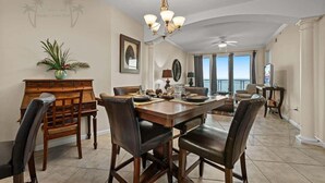 Uma ampla sala de jantar com uma grande mesa de madeira, cadeiras de couro e um candelabro.