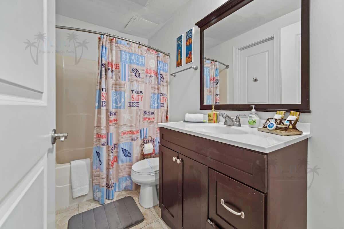 Un baño con cortina de ducha, inodoro, lavamanos con espejo y un armario.