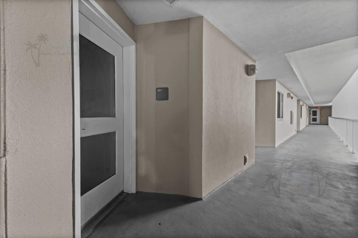 A long, narrow hallway with a beige wall, a door with a window, and a number plate.