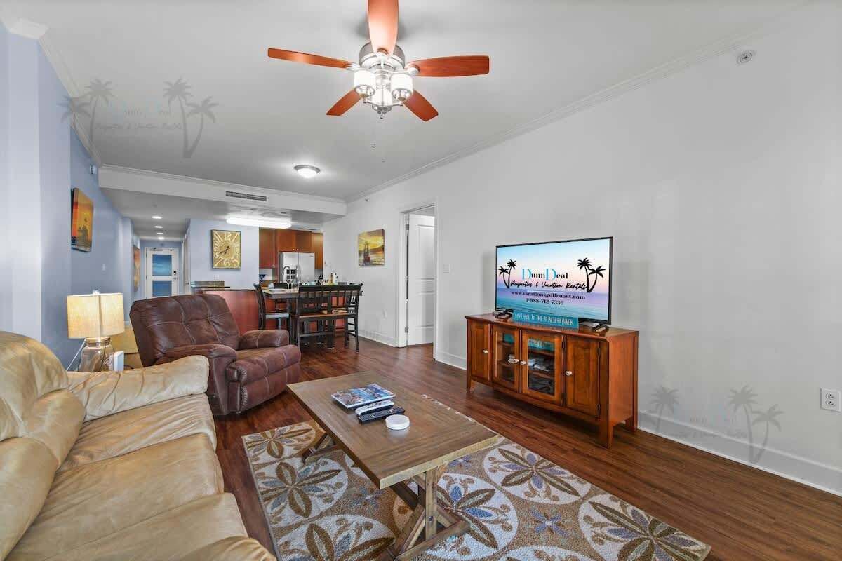 Un salon doté d’un ventilateur de plafond, d’un téléviseur, d’un canapé, d’une table basse et d’un tapis à motifs.