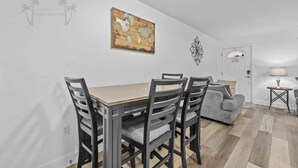 Ein Essbereich mit einem Holztisch, vier Stühlen, einem grauen Sofa und einer Wanddekoration.