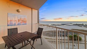 Un balcone con tavolo e sedie, affacciato su una spiaggia con vista sul tramonto.