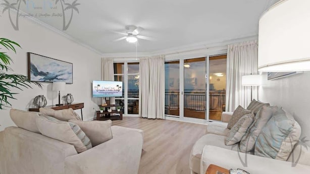 Ein geräumiges Wohnzimmer mit großem Fernseher, bequemen Sofas, einem Deckenventilator und einem Balkon mit Vorhängen.