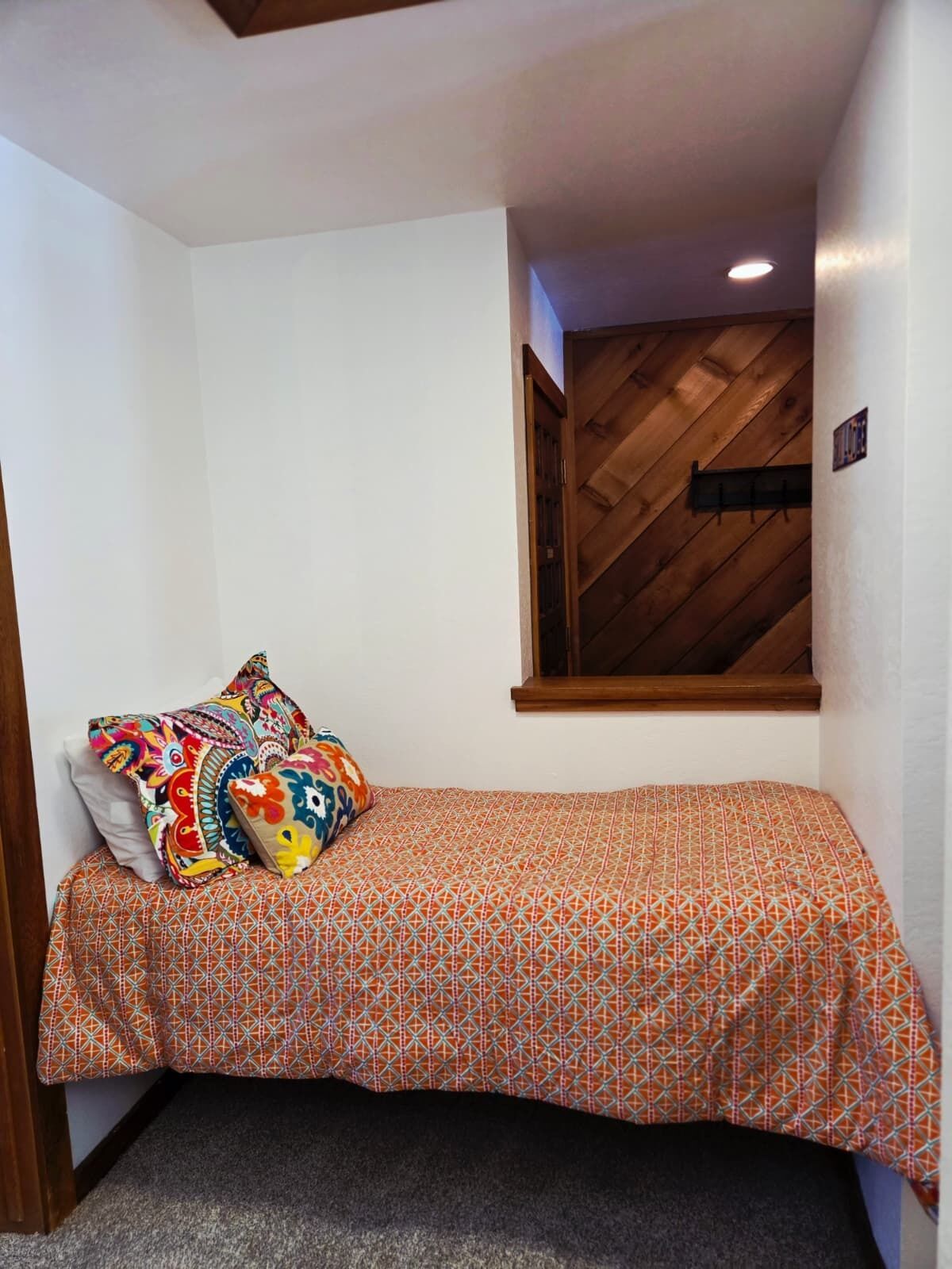 Una habitación pequeña y acogedora con una cama individual, almohadones coloridos y techo de madera.